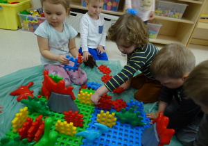 Dzieci układają na podłodze z klocków dinozaurowy świat.