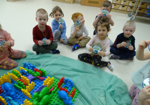 Dzieci siedzą na podłodze i pokazują medale z okazji Dnia Dinozaura.