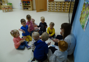 Dzieci siedzą na podłodze i wyklaskują sylaby.