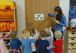 Dzieci stoją z nauczycielką i mrówką - gościem przy obrazku z krokodylami i liczą je.