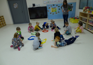 Dzieci siedzą w kole, na podłodze leżą kolorowe szarfy i pomieszane kolorowe węże.