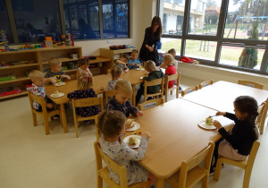 Dzieci siedzą przy stoliku i jedzą ciasto.