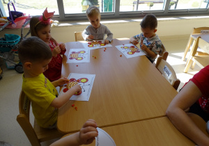 Dzieci siedzą przy stoliku i wyklejają plasteliną motyle.