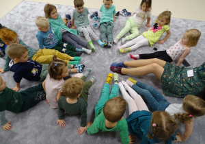 Dzieci z panią siedzą na podłodze w kole pokazując swoje kolorowe skarpetki.