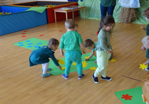 Dzieci układają na zielonych kartonach kolorowe kwiaty.