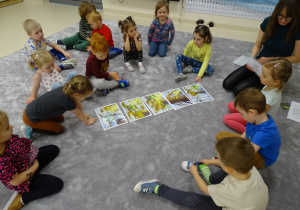 Dzieci siedzą w kole na podłodze i słuchają historii o wiosennym promyku czytanym przez panią.