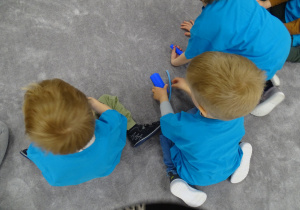 Dzieci siedzą na podłodze z niebieską bibułą i niebieskim drucikiem kreatywnym.