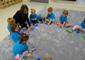 Dzieci siedzą na dywanie i wykonują pracę plastyczną z niebieskiej bibuły i niebieskiego drucika kreatywnego.