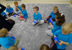 Dzieci siedzą na dywanie ze swoimi niebieskimi motylami.