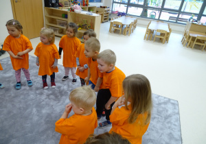 Dzieci z panią stoją w kole ubrane na pomarańczowo. Seba i Gabryś ćwiczą z marchewkami.