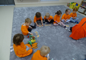 Dzieci siedzą w kole ubrane na pomarańczowo i rozkładają swoje wydrukowane marchewki..