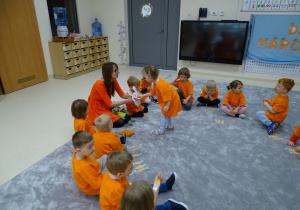 Dzieci siedzą w kole ubrane na pomarańczowo. Lena karmi królika.