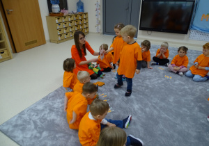 Dzieci siedzą w kole ubrane na pomarańczowo. Julka i Ernest karmią królika.