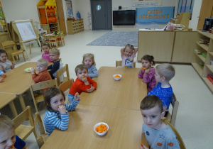Dzieci siedzą przy stolikach i częstują się marchewkami.