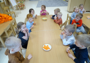 Dzieci siedzą przy stolikach i częstują się marchewkami.