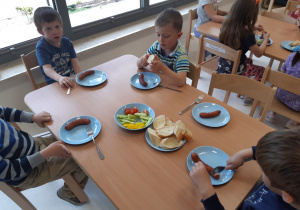 Dzieci jedzą kiełbaski z grilla