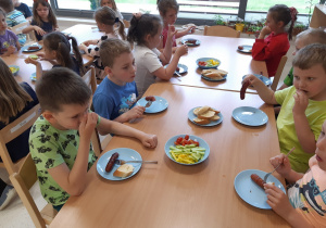 Dzieci jedzą obiad kiełbaski z grilla