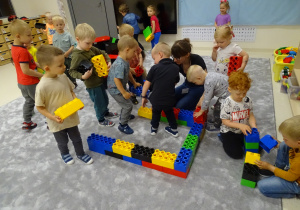 Dzieci budują dom z dużych klocków.