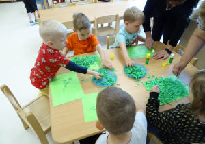 Dzieci wyklejają kartkę "trawą" z rozdrobnionej zielonej kartki.