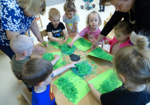 Dzieci wyklejają kartkę "trawą" z rozdrobnionej zielonej kartki.
