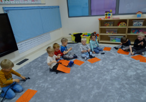 Dzieci siedzą na podłodze z sylwetami biedronek i robią kulki z bibuły.