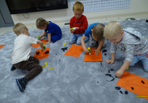 Dzieci przyklejają bibułę na sylwety biedronek.