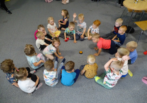 Dzieci siedzą w kole na podłodze.