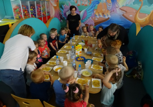 Dzieci siedzą przy stole i jedzą frytki.