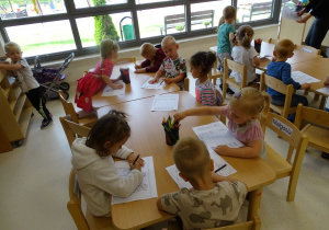 Dzieci siedzą przy stolikach i kolorują.