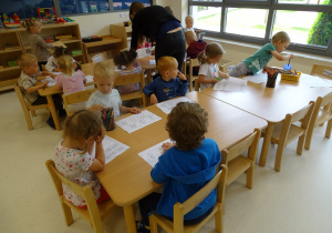 Dzieci siedzą przy stolikach i kolorują.