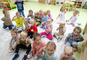 Dzieci siedzą na podłodze i pokazują, gdzie mają uszy.