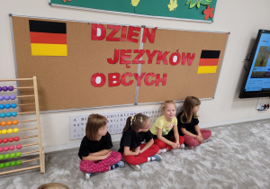 Dziewczynki ubrane w kolory flagi Niemiec siedzą pod tablicą