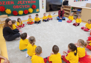 Dzieci w żółto-czerwonych barwach w kole wraz z uczniami liceum