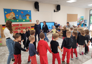 Dzieci z uczennicami tańczą w kole trzymając się za ręce