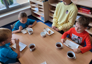 Dzieci wraz z uczniem liceum przy stoliku z herbatką i szarlotką