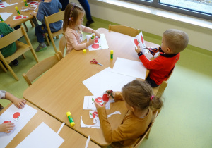 Dzieci siedzą przy stolikach i wycinają obrazki.