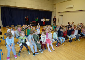 Dzieci siedzą tyłem do muzyków i odgadują zagadki poprzez podnoszenie rąk.