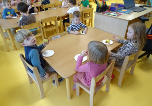 Dzieci siedzą przy stolikach i jedzą ciasto