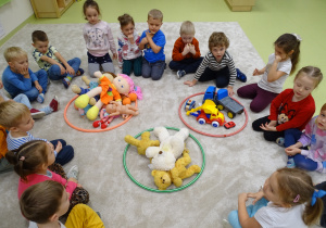 Dzieci siedzą w kole, w którym leżą 3 hula hop w różnych kolorach i sortują swoje zabawki wg rodzaju zabawki.