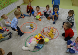 Dzieci siedzą w kole, w którym leżą 3 hula hop w różnych kolorach i sortują swoje zabawki wg wielkości zabawki.