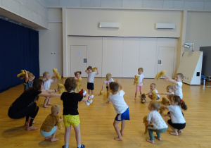 Dzieci ćwiczą na sali gimnastycznej ze swoimi misiami - przysiady.