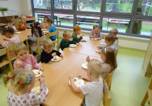Dzieci siedzą przy stolikach i jedzą tort.