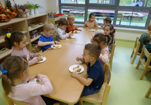 Dzieci siedzą przy stolikach i jedzą tort.