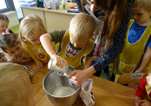 Kacper wsypuje mąkę do misy. Pozostałe dzieci obserwują.
