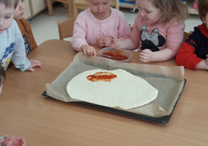 Dziewczynki smarują sosem pizzę