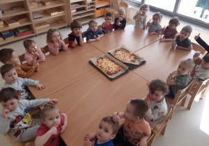 Dzieci siedzą przy stolikach, na stoliku leży upieczona pizza