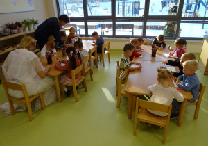 Dzieci siedzą przy stolikach i wykonują zadanie.