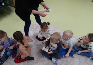 Dzieci siedzą na dywanie ze swoimi kartami otrzymanymi od pani bibliotekarki.