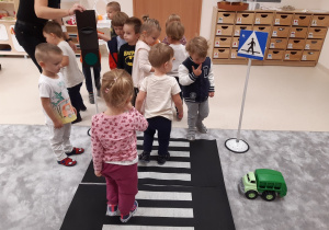 Dzieci uczą się przechodzić przez przejście dla pieszych na macie rozłożonej w sali