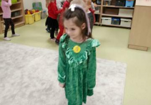 Dziewczynka w zielonej sukience stoi.
